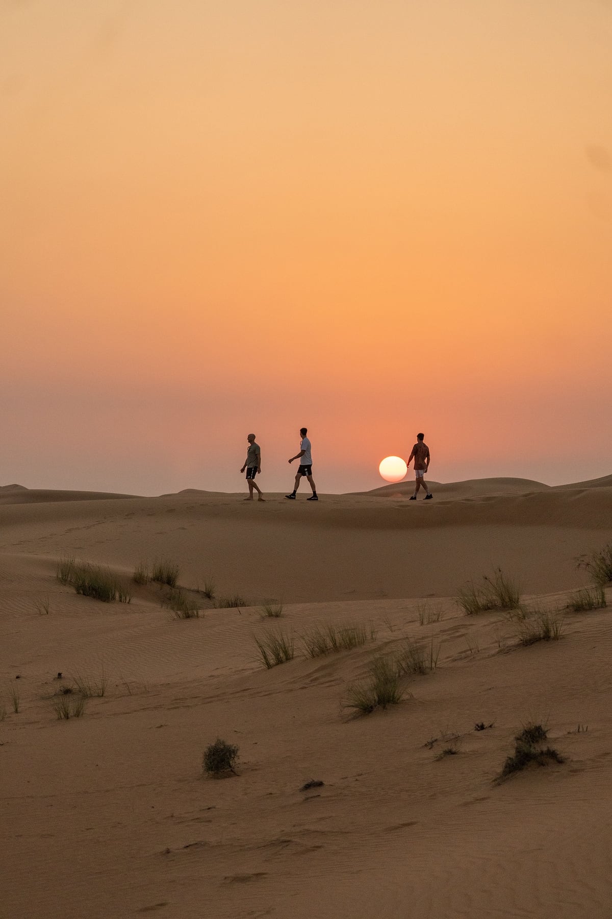 Three people walking along a dune ridge in the Dubai desert at sunset